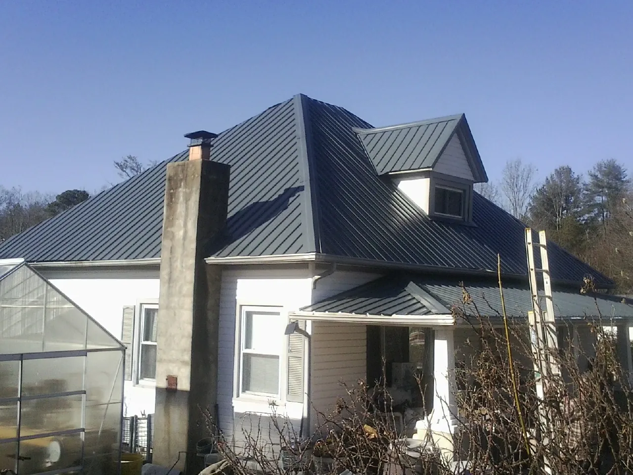 Dark blue standing seam metal roof on a white farmhouse with dormer — Slate & Tile Roof Repair by Roofing Brothers in Bolton