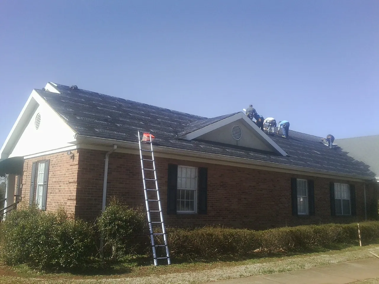 Crew tearing shingles off a brick ranch roof with a ladder set — Metal Roof Repair work by our crew in Bolton