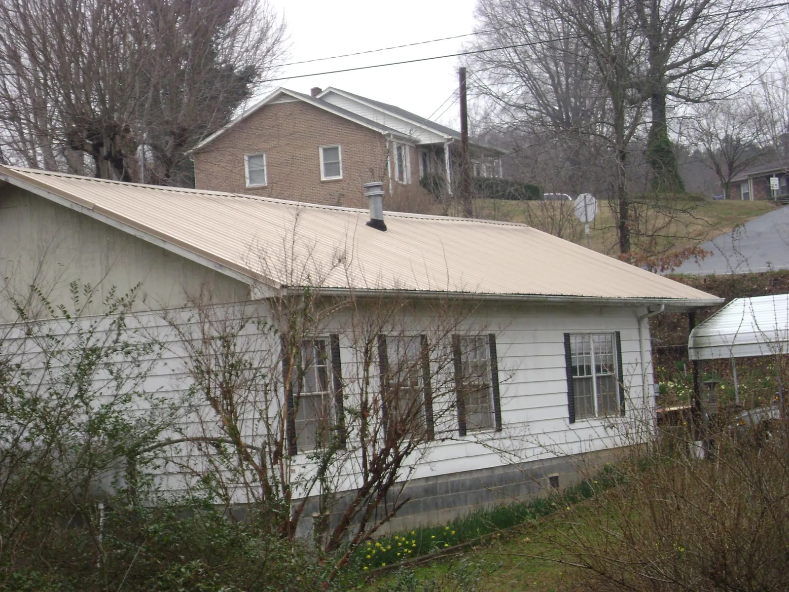 Tan metal roof on a white sided house set into a hillside — Commercial Roofing by Roofing Brothers in Bolton