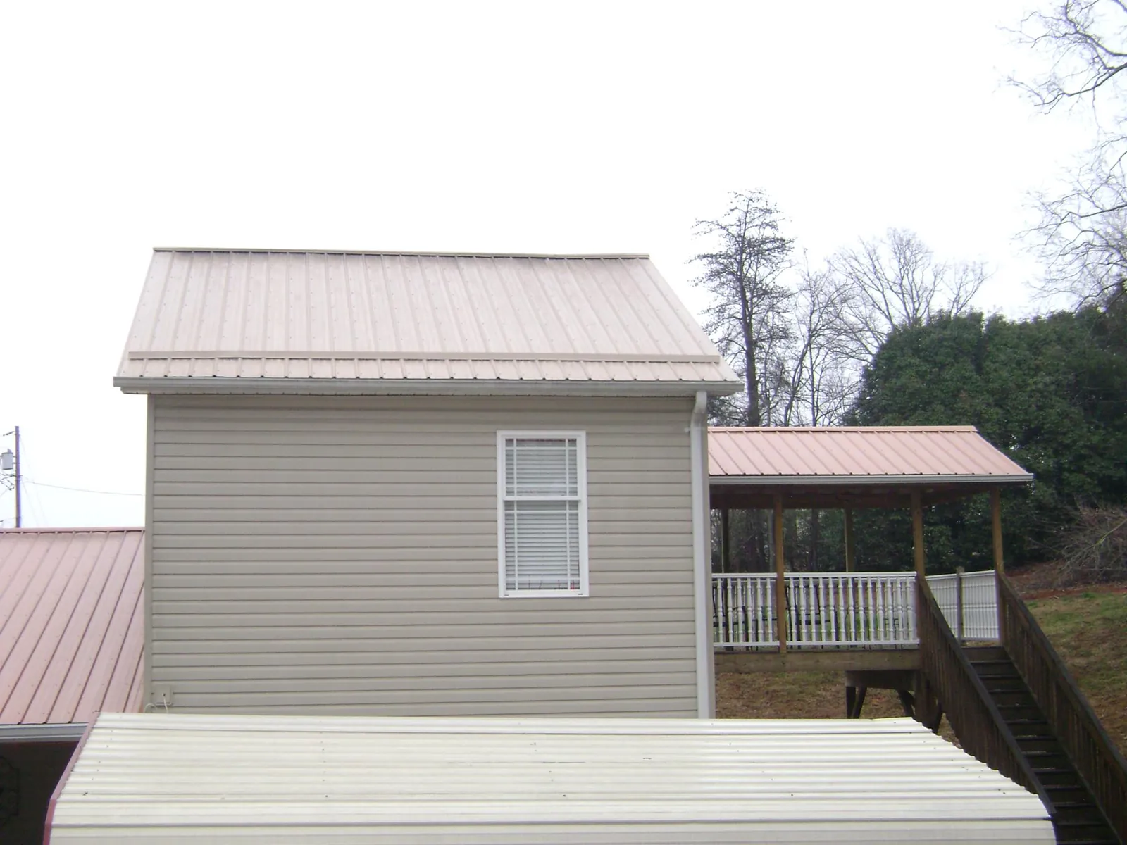 Tan metal roofs on a two story addition and attached porch, from a Roof Replacement job in Bolton